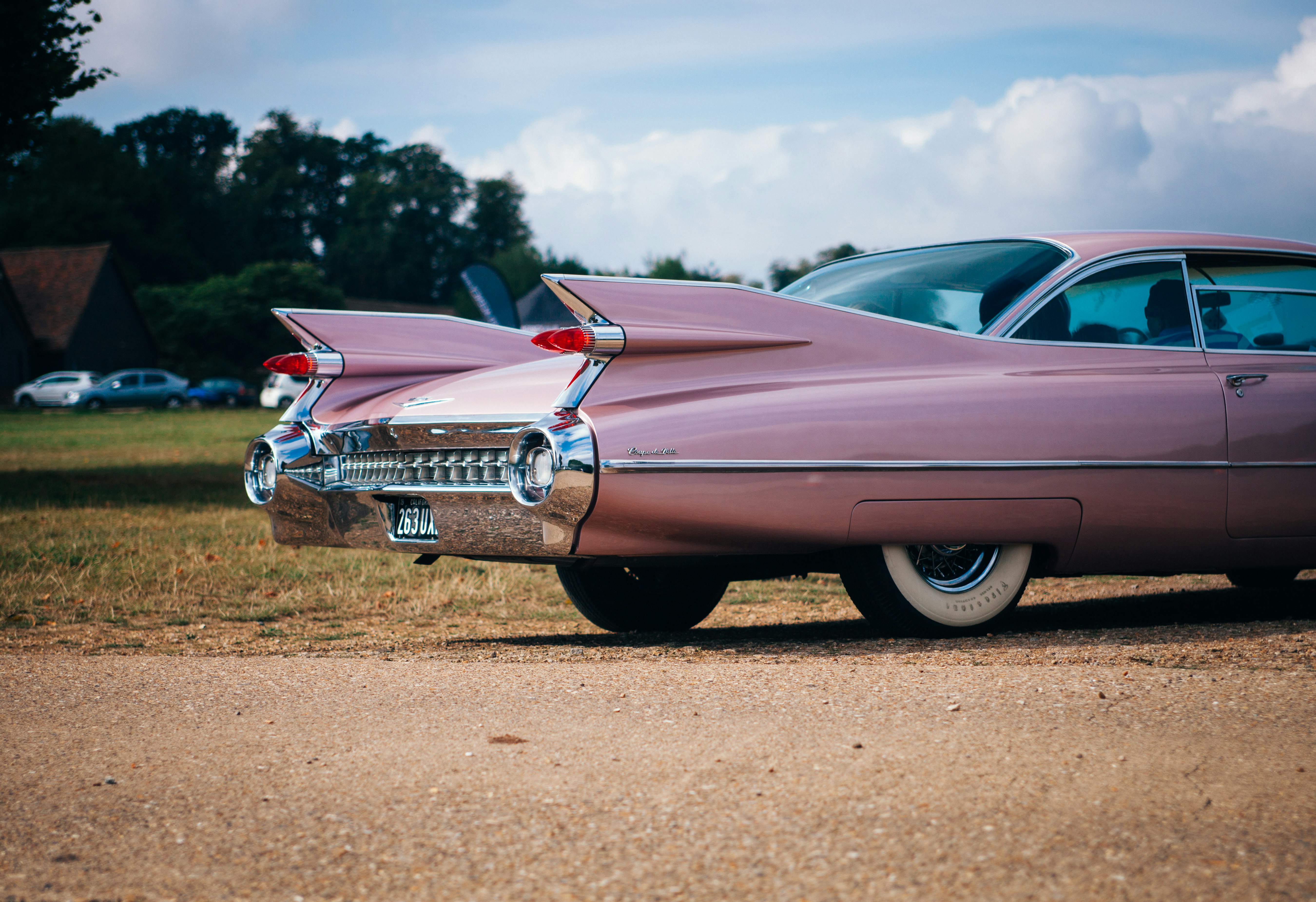 vintage pink muscle car parked near field of grass